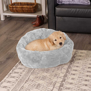 A black and brown dog lying on a gray spotted FurHaven pet bed in a living room on gray wood floor. 